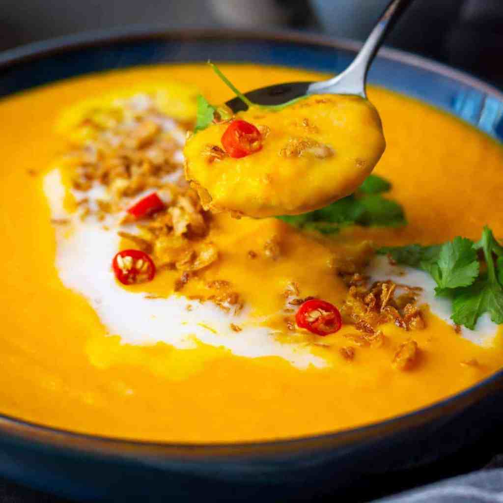 Silky carrot ginger soup with warm spices and a drizzle of coconut cream served in a rustic bowl