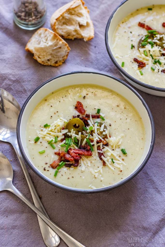 A bowl of creamy potato soup topped with chives, cheese, and bacon, accompanied by pieces of bread on the side.