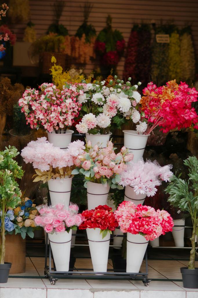 A display of colorful artificial flowers arranged in white pots at a flower shop.