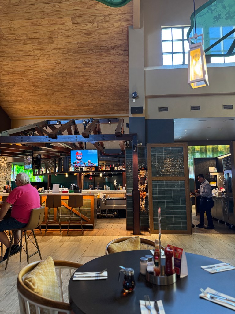 Interior view of a restaurant at Great Wolf Lodge, featuring wooden beams, a bar with various drinks, and tables set for dining.