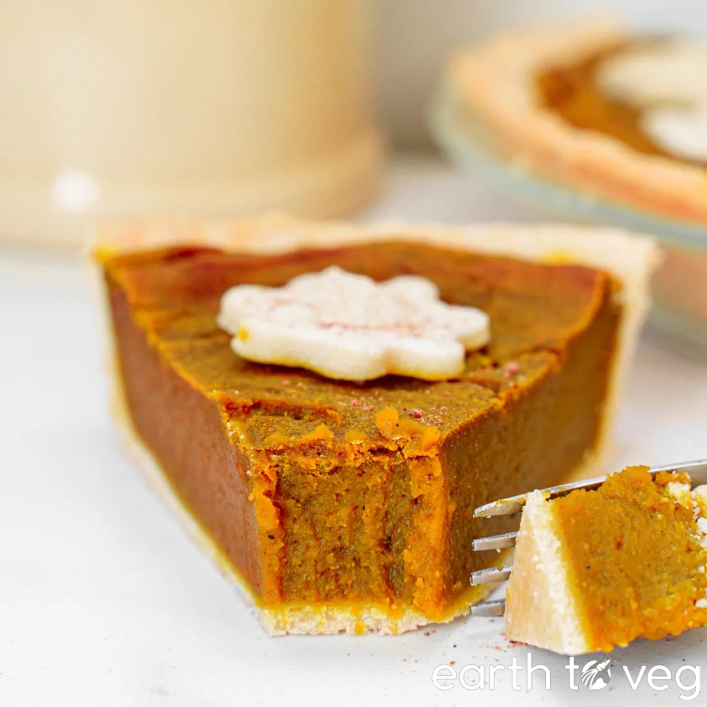 A slice of pumpkin pie topped with a decorative icing shape, showing the creamy pumpkin filling and flaky crust.