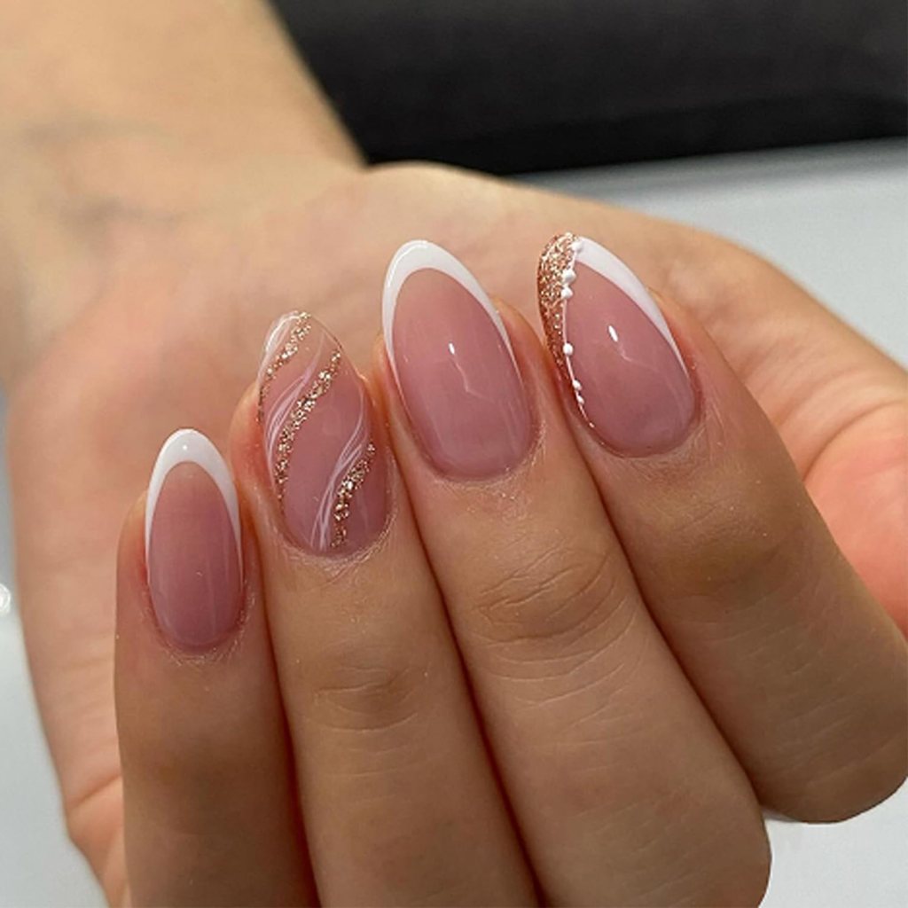 Close-up of a hand with manicured nails featuring a nude base, white tips, and gold glitter accents.
