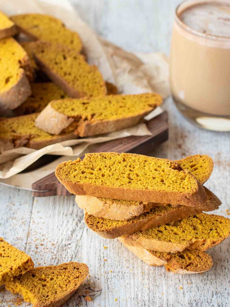 Sliced pumpkin biscotti arranged neatly with a glass of spiced drink in the background.