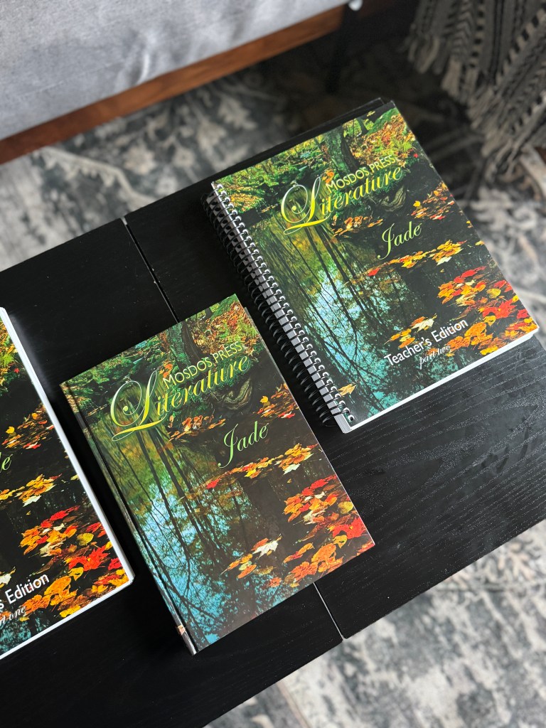 Two books titled 'Mosdos Press Literature: Jade' and 'Teacher's Edition' displayed on a black table, featuring a serene nature cover with trees and fallen leaves.