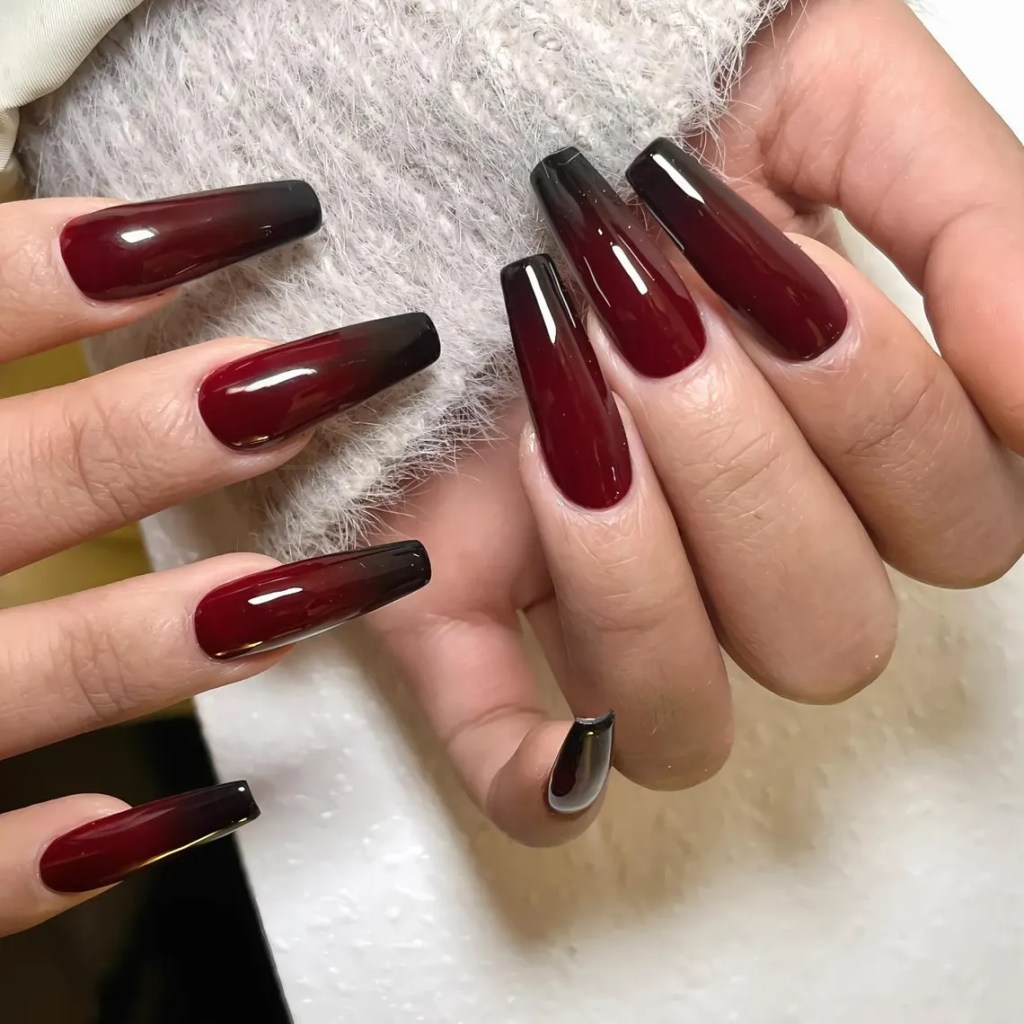 Close-up of hands displaying long, glossy burgundy nails with black tips, showcasing an elegant nail art design.