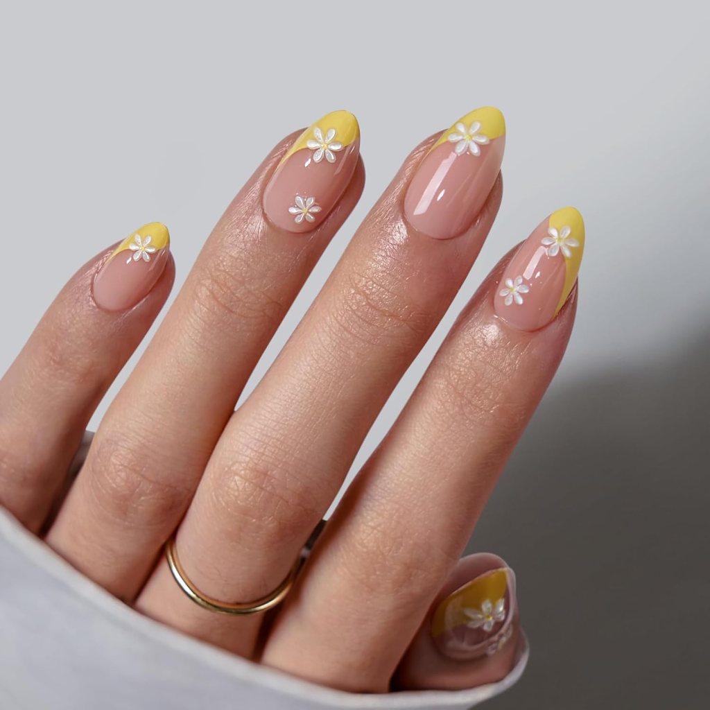 Close-up of a hand with elegantly manicured nails featuring yellow tips and white floral designs on a natural base.