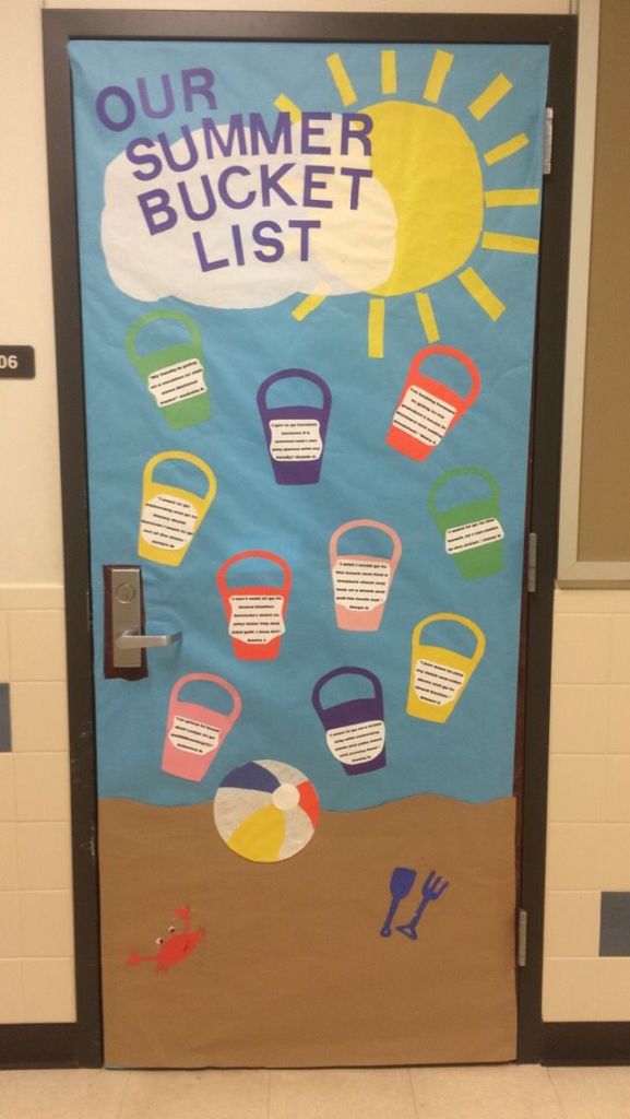 A decorated school door with a summer theme, featuring the text 'OUR SUMMER BUCKET LIST' in large letters at the top. Below, colorful beach buckets are displayed along with various listed summer activities. There is a beach ball illustration and small images of a crab and sand tools at the bottom.