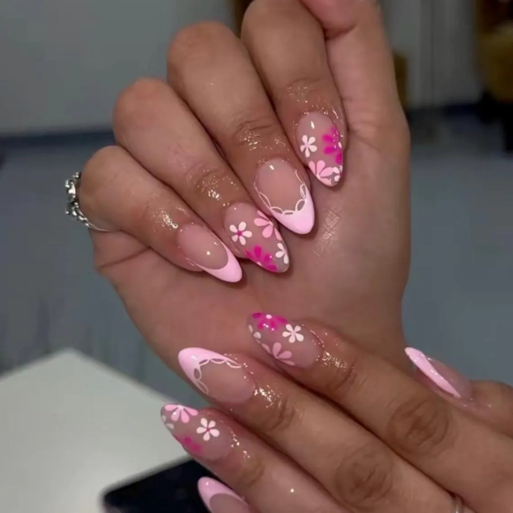A close-up view of a hand displaying elegantly manicured nails with a combination of pink and clear nail polish, featuring floral designs in white and pink on the tips.