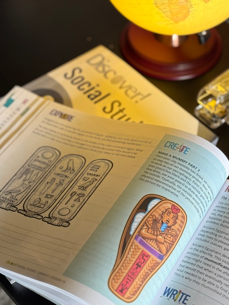 An open page from the Discover! Social Studies Grade 6 curriculum showcasing a lesson on Ancient Egypt, featuring illustrations of Egyptian hieroglyphics and a mummy sarcophagus. A globe is illuminated in the background.