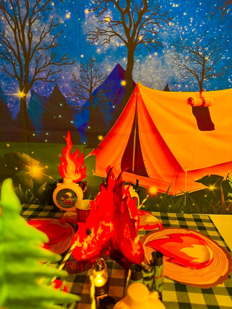 Camping party centerpiece with faux fire, tent backdrop, and lanterns for a kids birthday party.