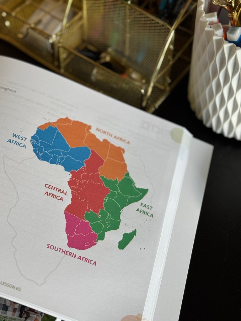 A colorful map of Africa segmented into regions: North Africa, West Africa, Central Africa, East Africa, and Southern Africa, displayed on a desk with stationery items in the background.