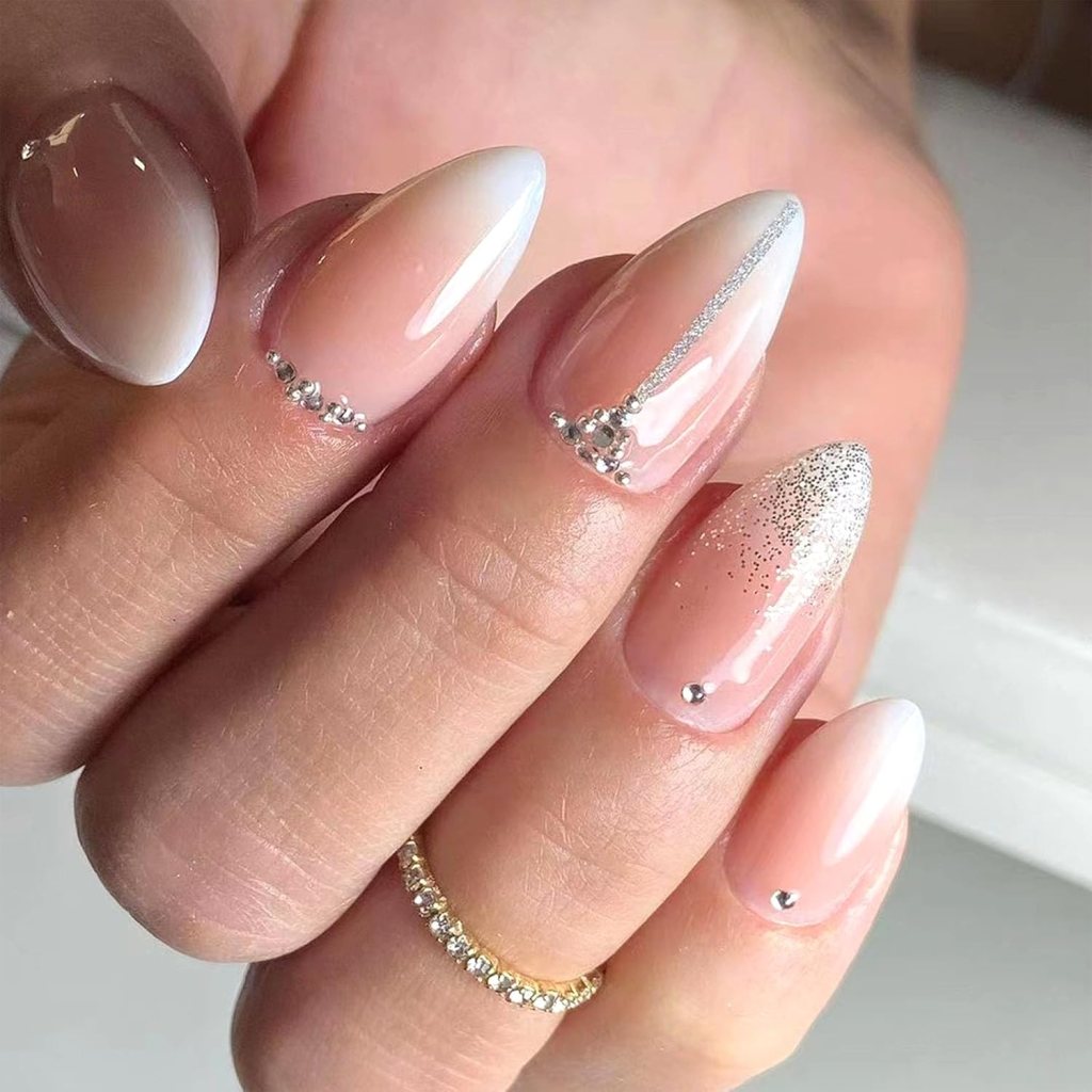 Close-up of manicured nails featuring a gradient design in light pink and white, accented with silver details and rhinestones.