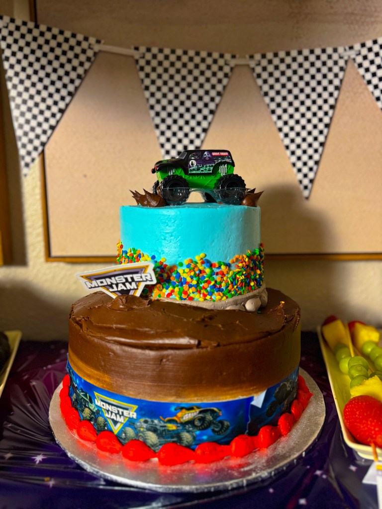 Monster Jam birthday cake with toy monster truck topper and colorful sprinkles on a racing themed dessert table.