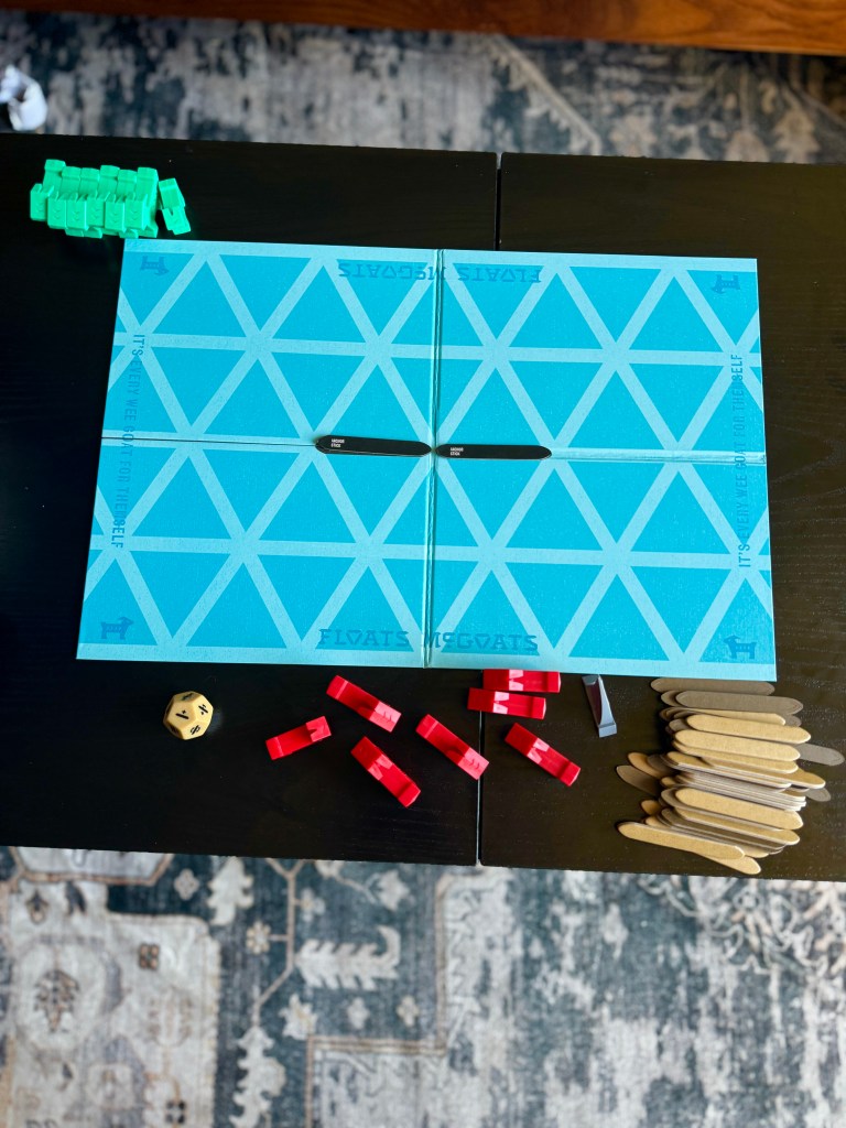 A game board featuring a blue surface with a diamond pattern, surrounded by game pieces including green and red tokens, a yellow dice, and wooden sticks, arranged on a dark table.