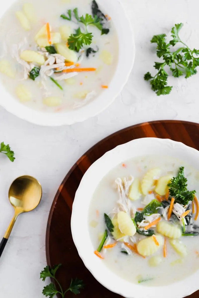 A bowl of creamy chicken and gnocchi soup featuring shredded chicken, gnocchi, colorful vegetables, and garnished with fresh parsley, served in a white bowl.