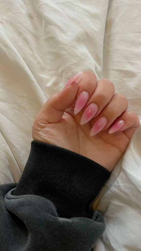 Close-up of a hand with long, pointed pink nails resting on a white bed sheet.