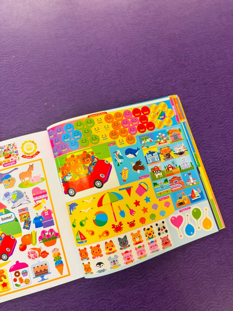 A colorful sticker book featuring various designs including animals, food, nature, and happy faces, placed on a purple surface.
