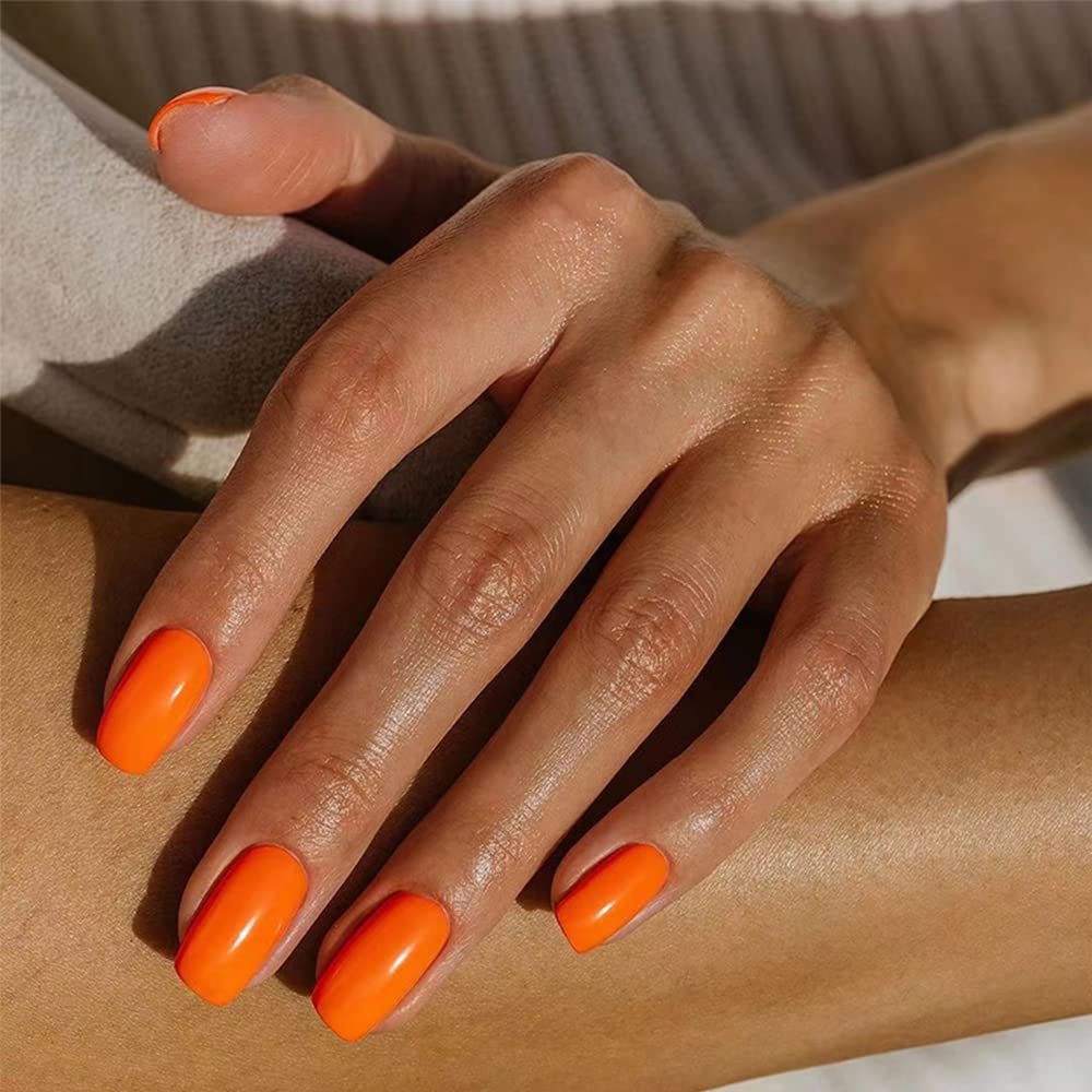Short nails painted in bright orange polish with glossy top coat