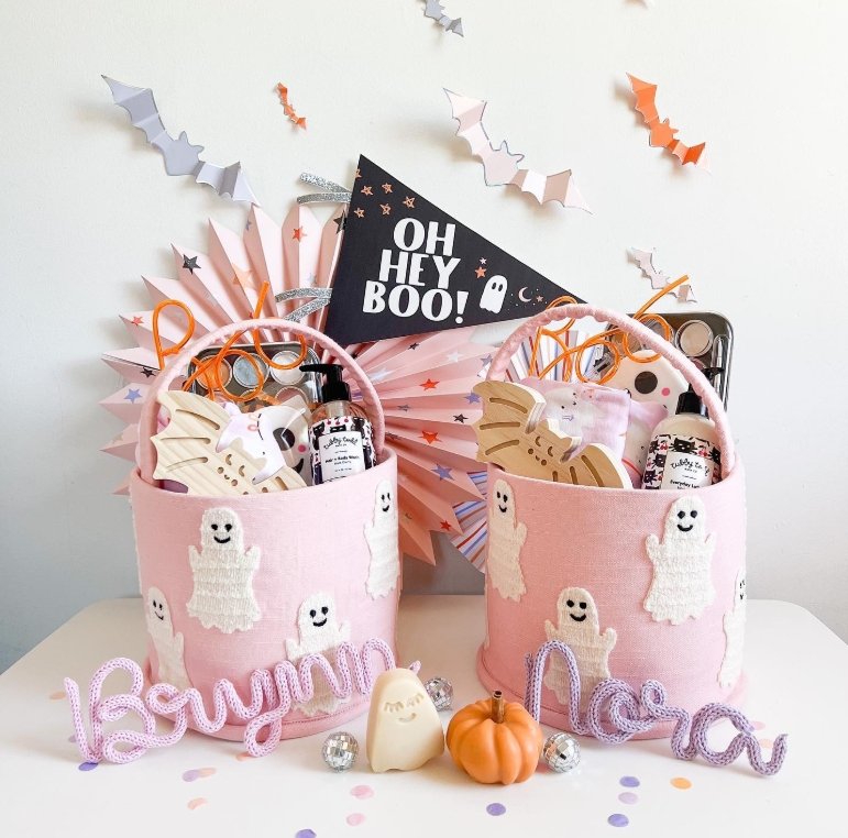 Two pink Halloween boo baskets decorated with ghost appliques, filled with treats and goodies, alongside a 'Oh Hey Boo!' banner and colorful decorations.