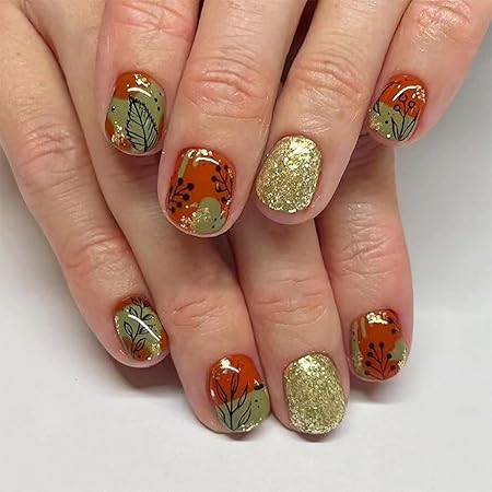 Autumn-themed nail design featuring orange and green colors with floral patterns, complemented by a golden glitter accent nail.