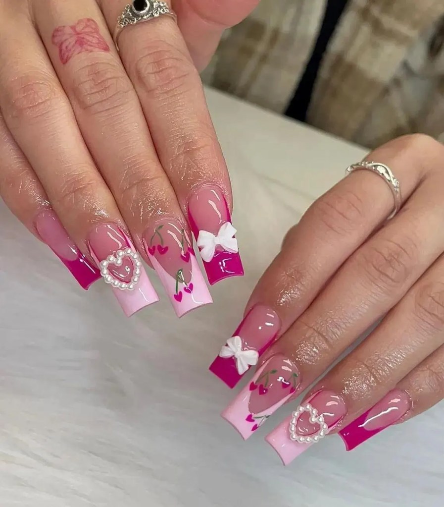 Close-up of beautifully manicured nails featuring a gradient from pink to vibrant berry, adorned with small heart designs, floral patterns, and decorative bows.