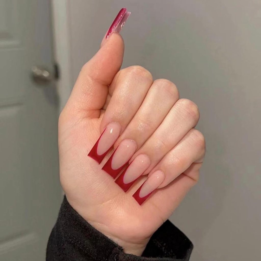 A hand displaying long almond-shaped nails with a gradient design, featuring a clear base that transitions into a deep red tip.