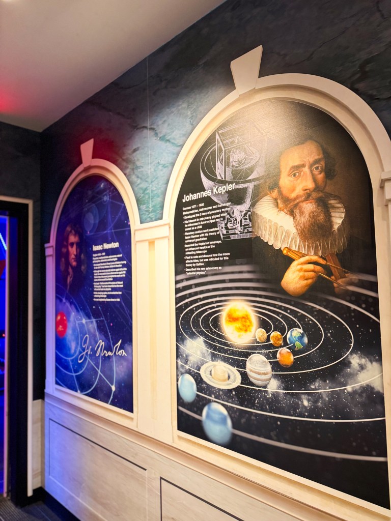 Artistic wall display featuring portraits of Isaac Newton and Johannes Kepler, with descriptions of their contributions to astronomy and an illustration of the solar system.