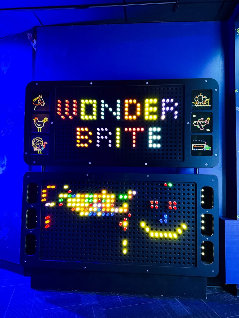A brightly-lit display board with the words 'WONDER BRITE' in colorful lights, featuring various animated patterns and characters on a dark background.