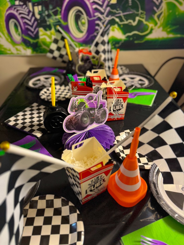 Monster Jam birthday party table setup with checkered racing plates, monster truck centerpiece, traffic cone cups, and themed snack boxes.