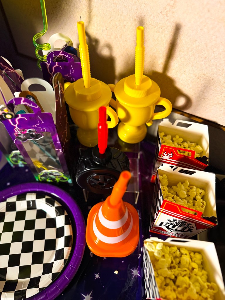 Monster Jam birthday party drink station with racing themed cups, monster truck party favors, popcorn boxes, and traffic cone decoration.