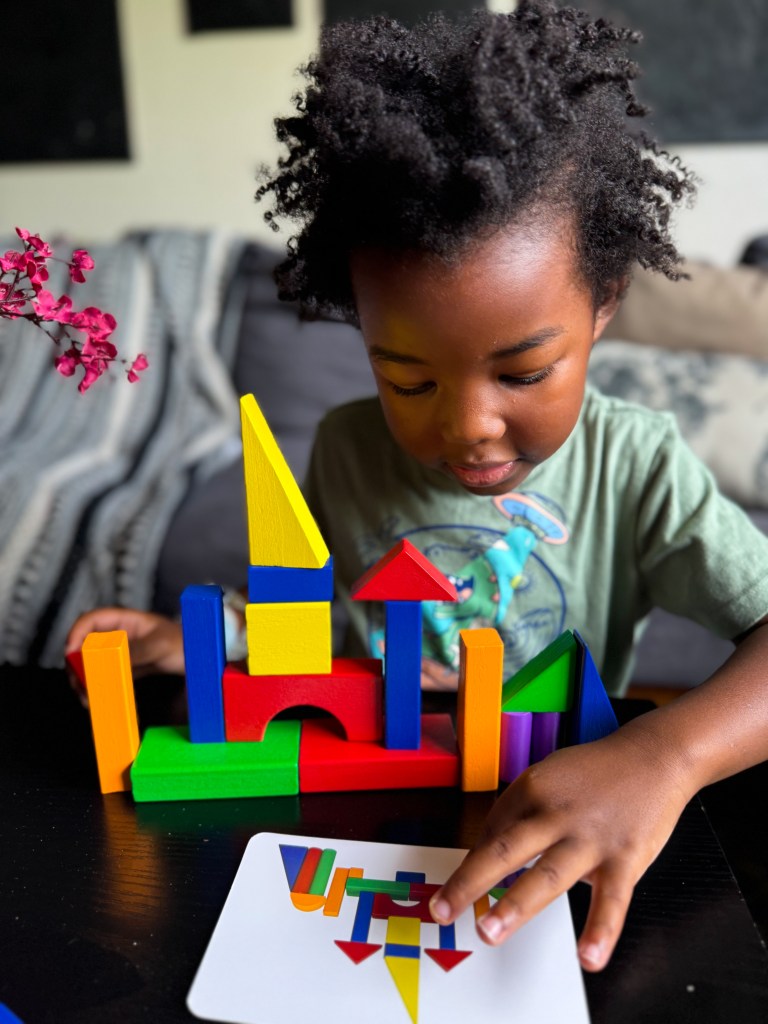 A young child playing with colorful building blocks, focused on arranging them to match a design shown on a card.