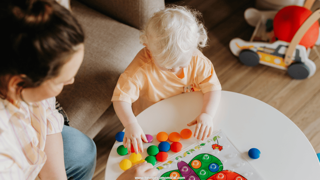 Toddler doing a colorful matching activity at a white table with an adult nearby during a learning activity for 2 year olds.