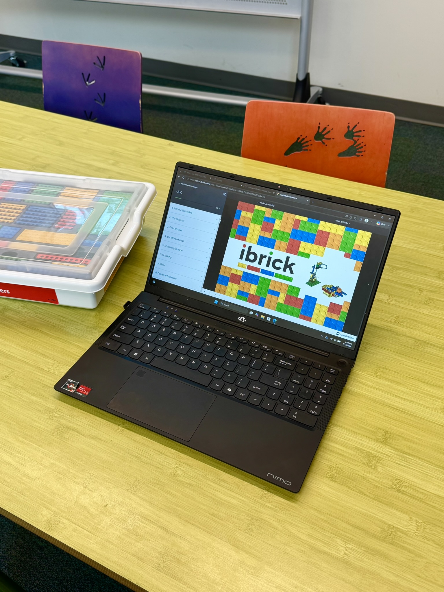 Laptop on a yellow table displaying 'ibrick' webpage with colorful building blocks and a plastic container of building bricks next to it