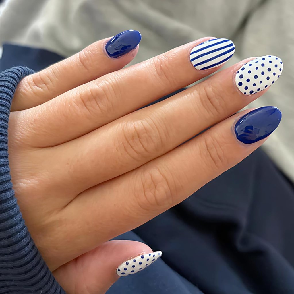 Navy blue striped and polka dot almond nails with glossy blue and white mix-match nail art.