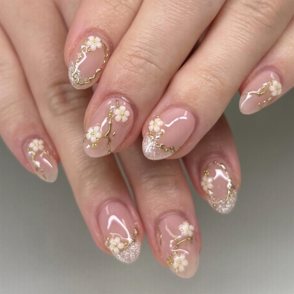 Close-up of elegantly manicured nails featuring a nude polish with white flower designs and gold accents.
