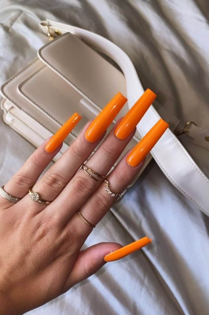 Long coffin nails painted in bright orange polish with glossy finish