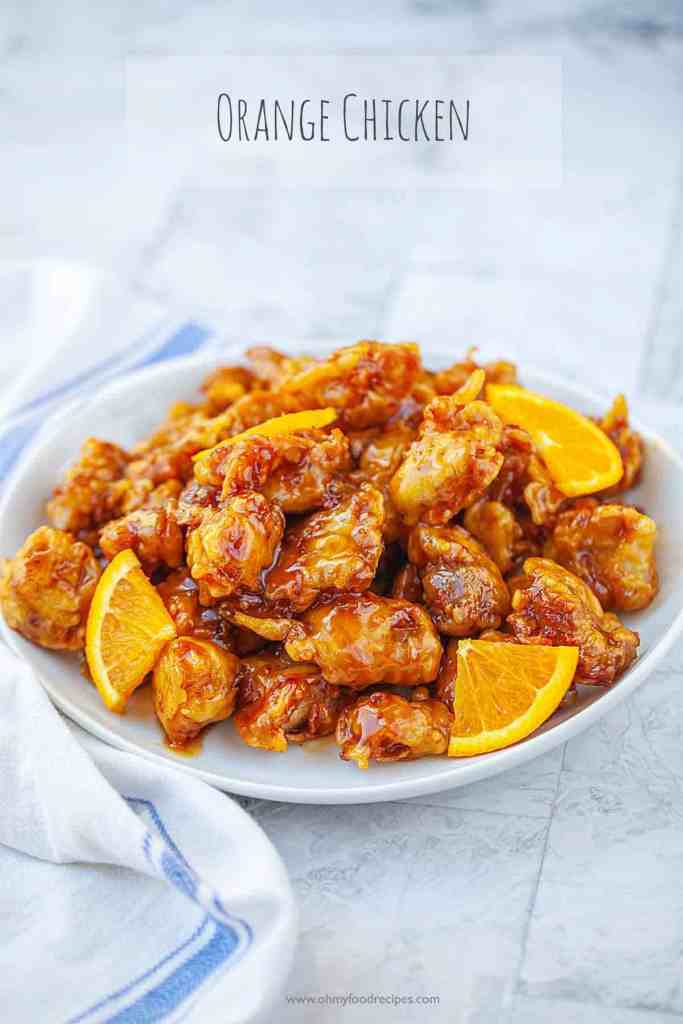 A plate of orange chicken garnished with orange slices, featuring crispy, golden-brown pieces coated in a sweet and tangy orange sauce, set against a light background.