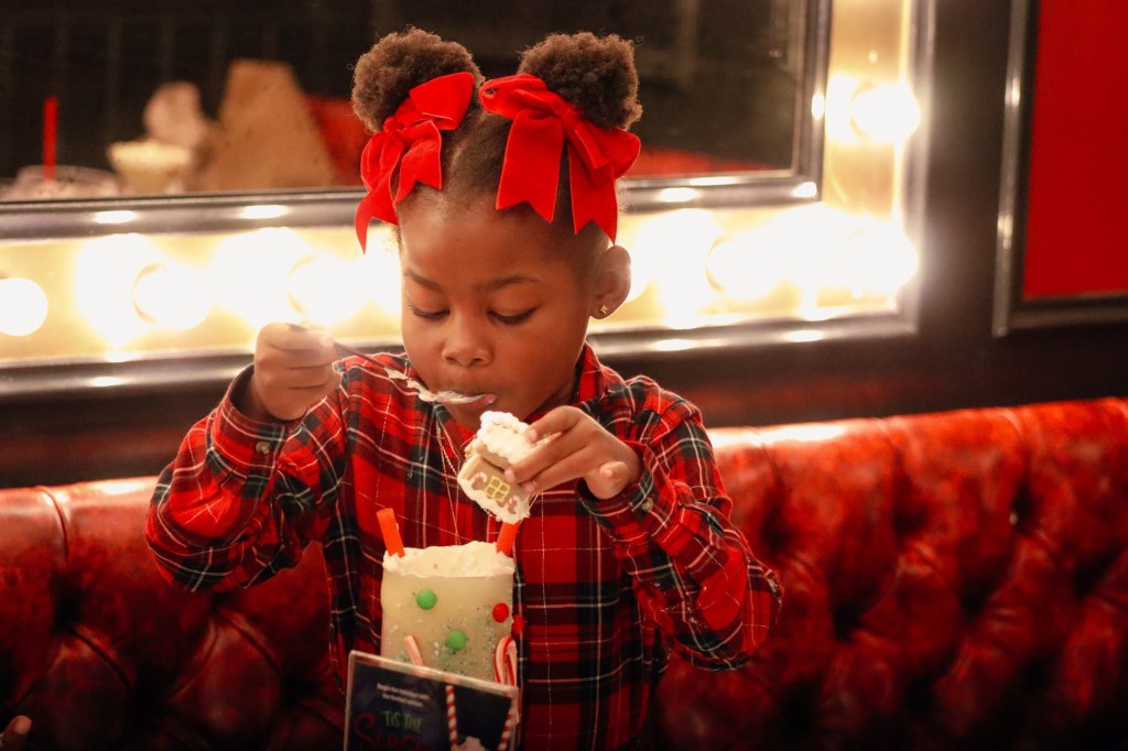 Young girl removing the miniature gingerbread house from Sugar Factory Biloxi's festive Christmas milkshake during a family holiday visit.