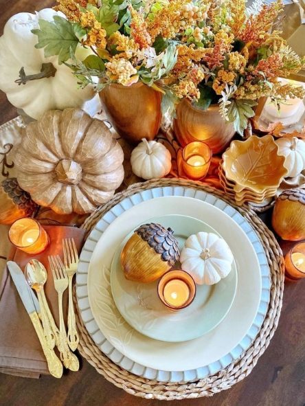 A cozy fall tablescape featuring various pumpkins, acorns, and seasonal flowers arranged with warm candlelight and elegant dinnerware, creating an inviting atmosphere.