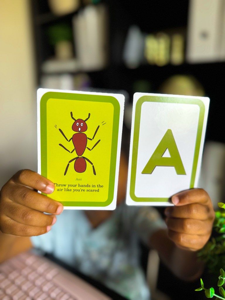 Child holding letter A and ant action cards during a kindergarten phonics activity