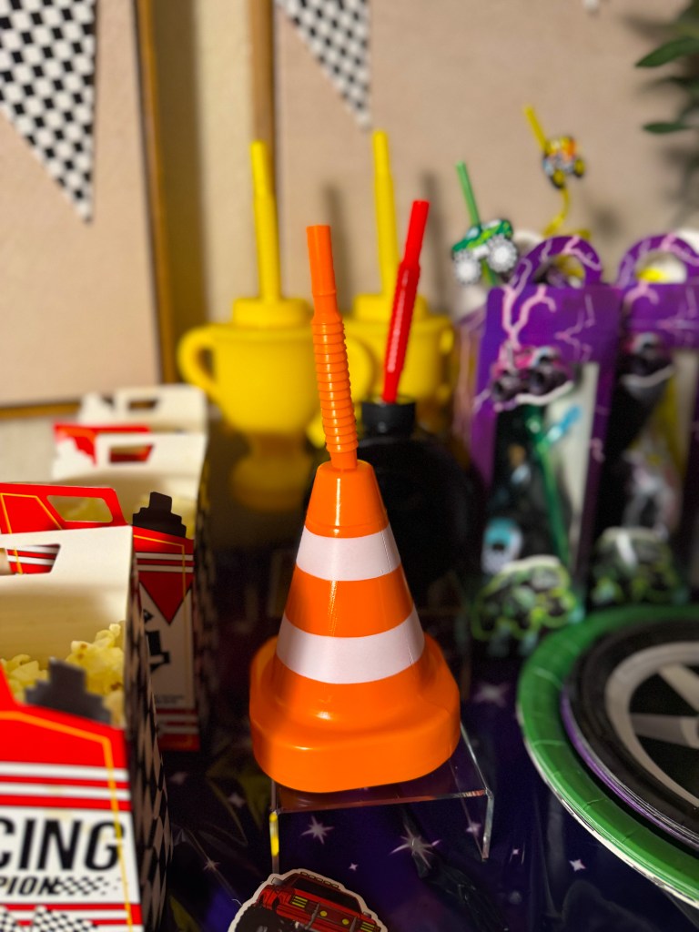 Colorful table display featuring an orange traffic cone with drinking straws, surrounded by yellow cups, popcorn boxes, and festive decorations.