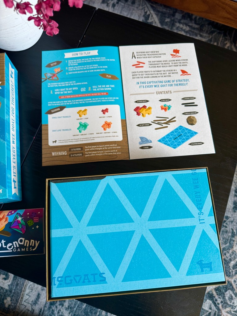 A colorful game box and instruction sheets on a wooden table, featuring the game 'Goats'. The instructions explain how to play the strategy game and include illustrations of game pieces.