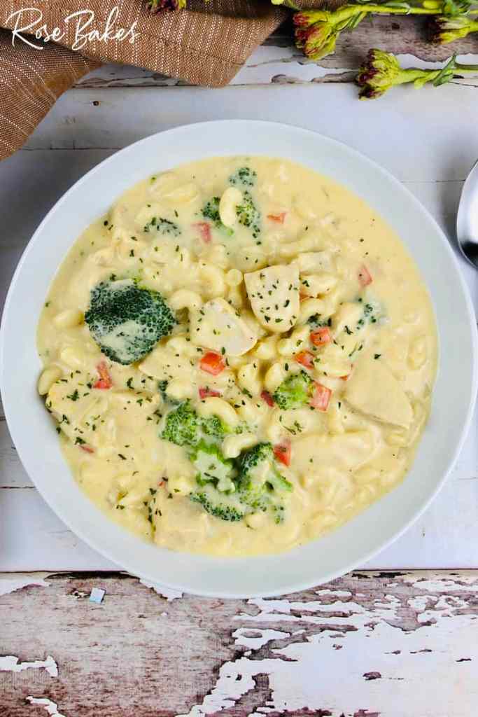 A bowl of creamy chicken and broccoli macaroni soup with diced chicken, broccoli florets, and colorful diced vegetables, garnished with herbs.