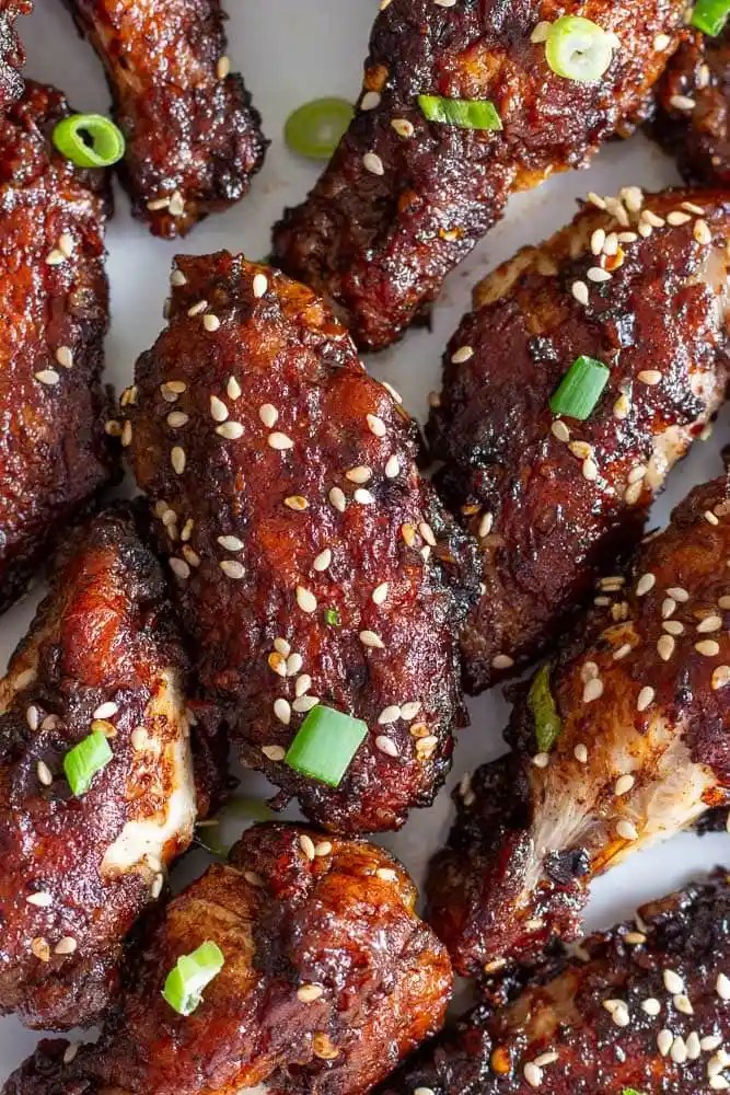 Close-up of crispy chicken wings garnished with sesame seeds and green onions, showcasing a golden-brown glaze.