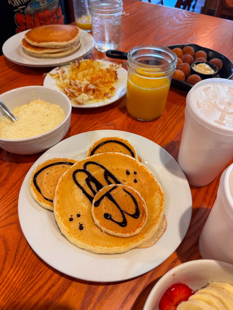 Family breakfast spread featuring pancakes, crispy hash browns, creamy grits, orange juice, and cinnamon-sugar fritters.