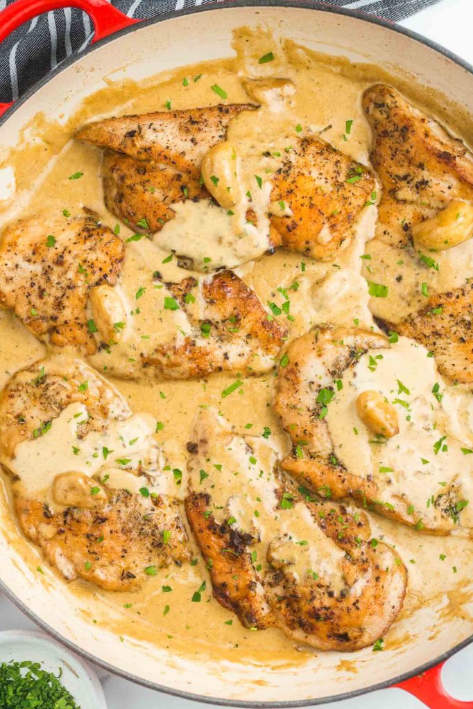 Seared chicken breasts in a creamy garlic sauce, garnished with fresh herbs in a skillet.
