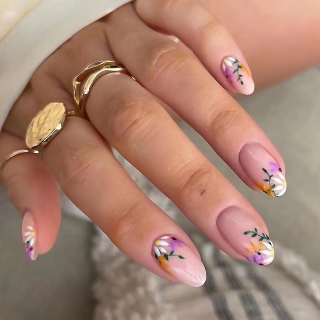 Close-up of a hand showing manicured nails with floral designs in pastel colors, surrounded by gold rings.