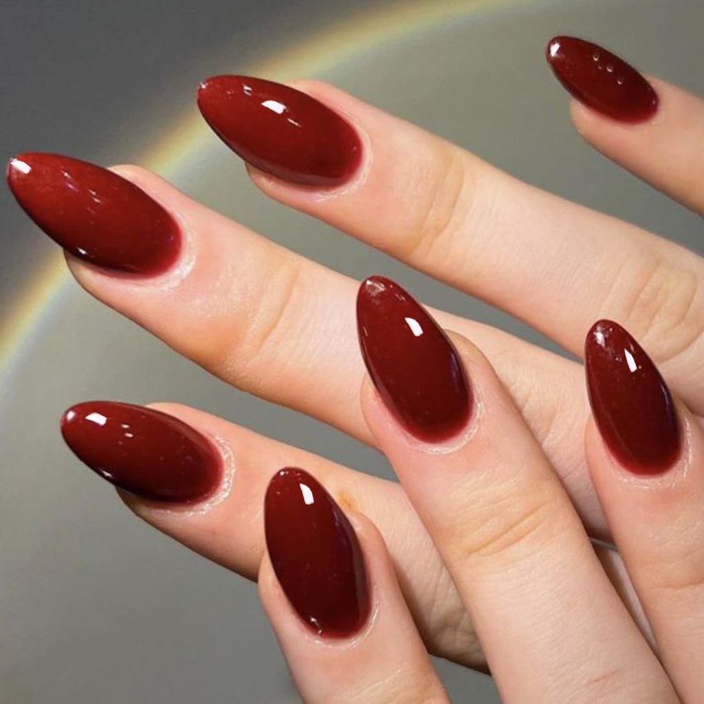 Close-up of fingers with long, almond-shaped nails painted in a glossy dark red polish.