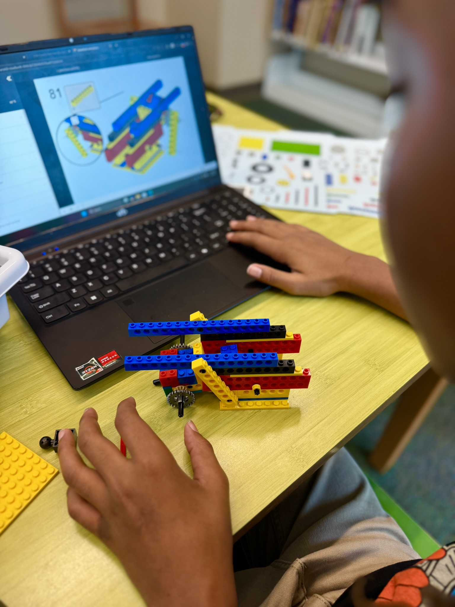 Child building a LEGO structure while following digital instructions on a laptop screen