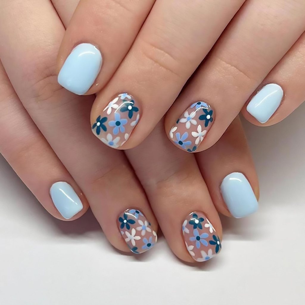 Close-up of hands with light blue nail polish and floral nail art featuring blue and white flowers on a clear background.